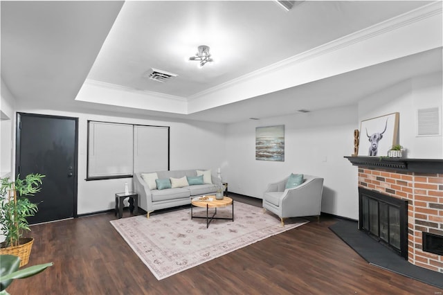 living room featuring a raised ceiling, crown molding, a brick fireplace, and dark hardwood / wood-style floors