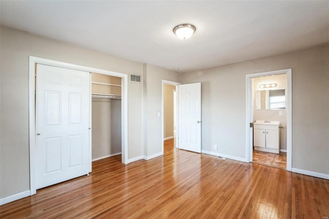 unfurnished bedroom with ensuite bathroom, light hardwood / wood-style floors, and a closet