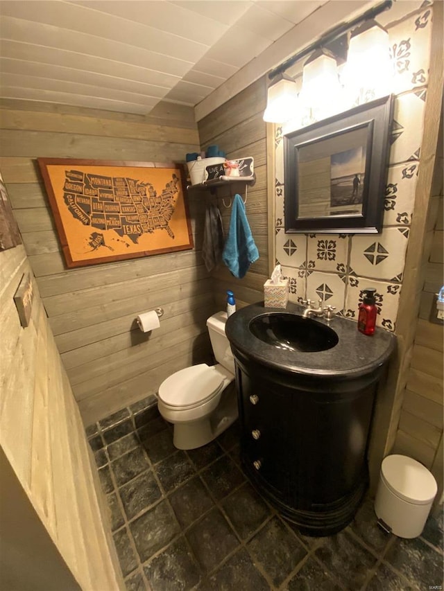 bathroom with vanity, wooden walls, and toilet