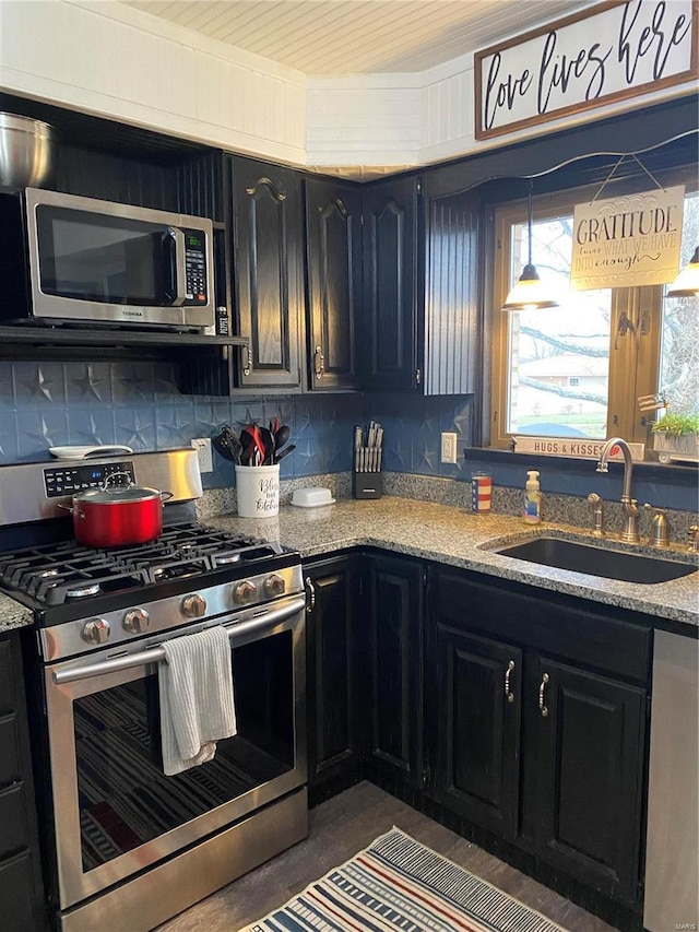 kitchen with decorative light fixtures, sink, backsplash, light stone counters, and stainless steel appliances