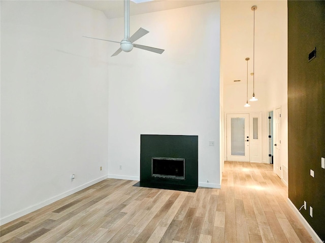 unfurnished living room featuring ceiling fan, a high ceiling, and light wood-type flooring