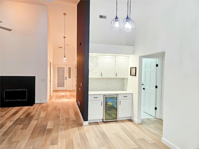 kitchen with white cabinets, light hardwood / wood-style flooring, wine cooler, and decorative light fixtures