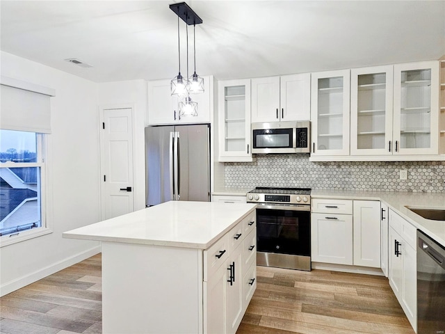 kitchen featuring white cabinetry, a center island, hanging light fixtures, stainless steel appliances, and light hardwood / wood-style floors