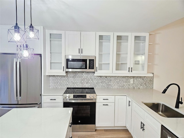 kitchen with sink, appliances with stainless steel finishes, white cabinetry, hanging light fixtures, and light stone countertops