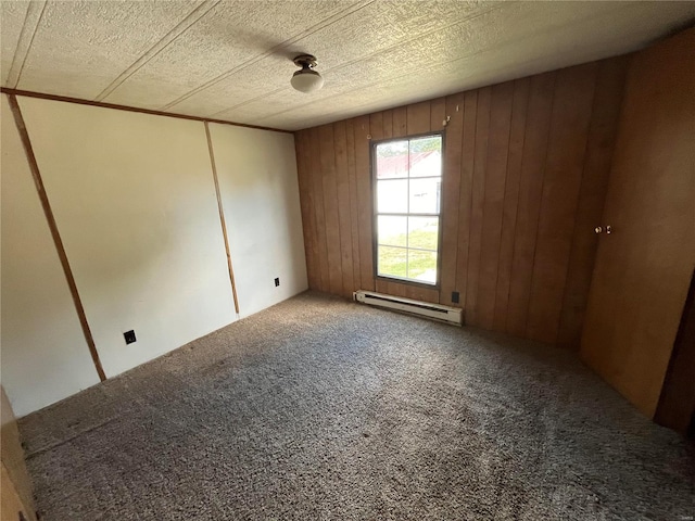 carpeted empty room featuring a textured ceiling, baseboard heating, and wood walls