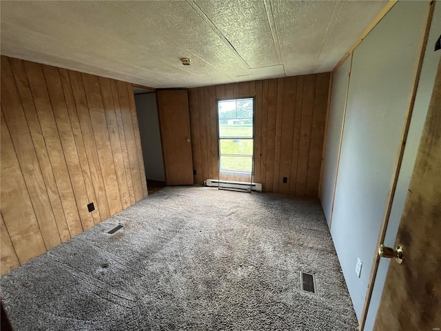 carpeted empty room with a baseboard radiator, a textured ceiling, and wooden walls