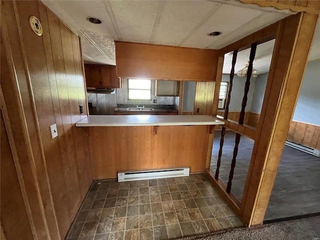 kitchen featuring baseboard heating, wooden walls, kitchen peninsula, and sink