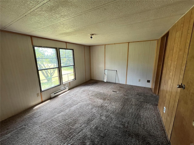 empty room with a baseboard heating unit, wooden walls, a textured ceiling, and carpet flooring