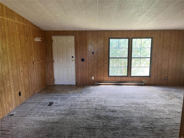 carpeted spare room with a baseboard heating unit and wooden walls