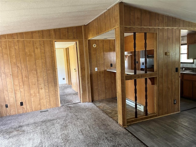 empty room featuring a baseboard heating unit, dark wood-type flooring, vaulted ceiling, and wooden walls