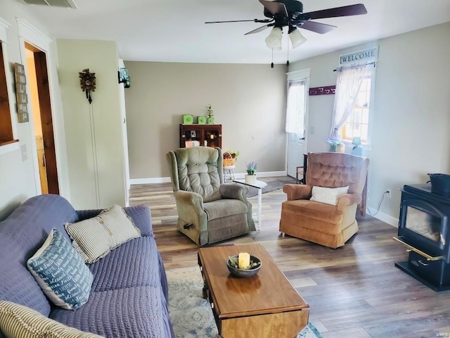 living room featuring ceiling fan, wood-type flooring, and a wood stove