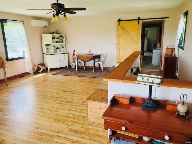 miscellaneous room featuring a barn door, a wall mounted AC, ceiling fan, and light hardwood / wood-style flooring