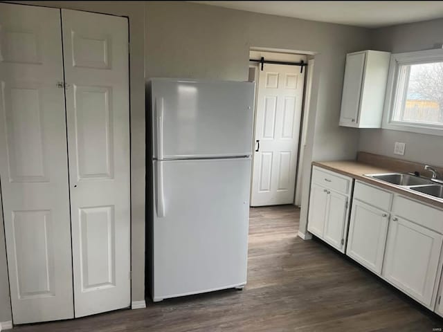 kitchen with sink, dark hardwood / wood-style floors, white refrigerator, white cabinets, and a barn door