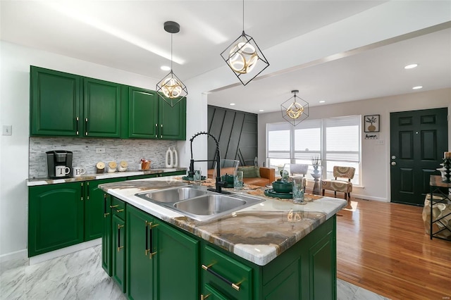 kitchen with a kitchen island with sink, hanging light fixtures, sink, and green cabinetry