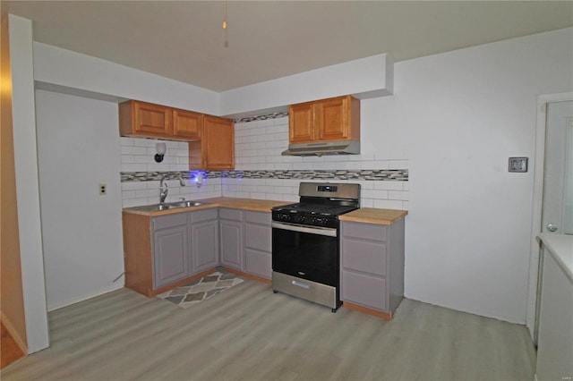 kitchen with light wood-type flooring, sink, decorative backsplash, and stainless steel gas range oven