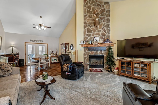 living room with a stone fireplace, high vaulted ceiling, hardwood / wood-style flooring, ceiling fan, and french doors