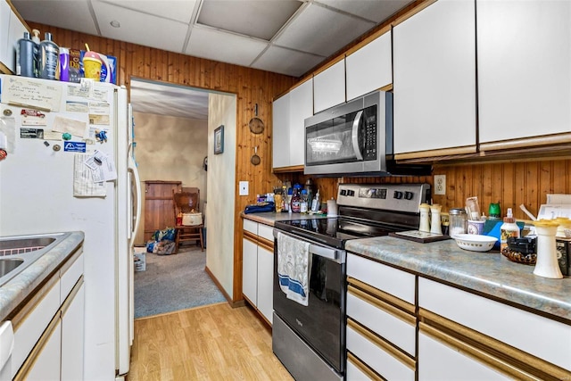 kitchen featuring appliances with stainless steel finishes, light hardwood / wood-style floors, white cabinets, a drop ceiling, and wood walls