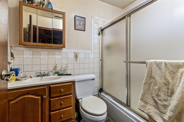 full bathroom featuring bath / shower combo with glass door, vanity, toilet, and tile walls