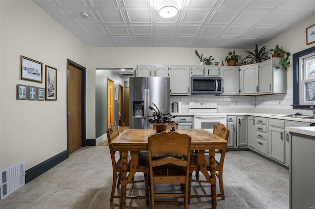 kitchen with gray cabinetry, backsplash, stainless steel appliances, and sink