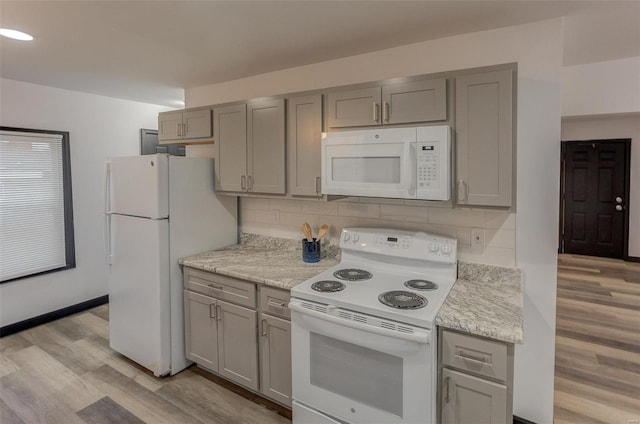 kitchen with tasteful backsplash, light stone countertops, white appliances, and light hardwood / wood-style flooring