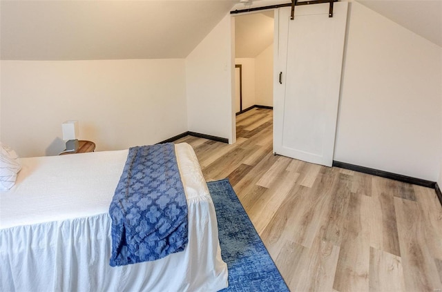 bedroom featuring lofted ceiling, a barn door, and light wood-type flooring