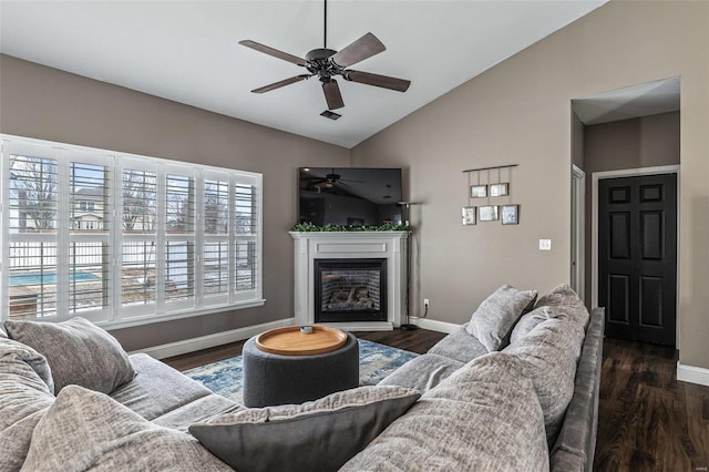 living area featuring dark wood-style floors, a glass covered fireplace, vaulted ceiling, and baseboards