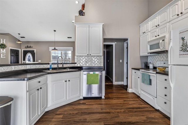 kitchen with dark countertops, hanging light fixtures, white cabinets, a sink, and white appliances