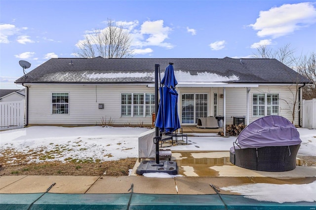snow covered house with roof with shingles, a patio area, fence, and an outdoor pool