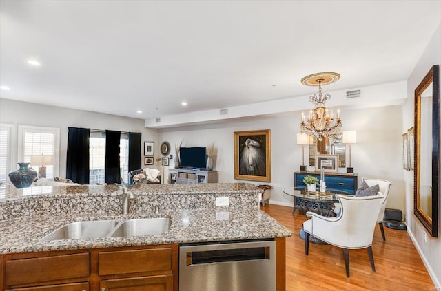 kitchen featuring sink, light wood-type flooring, stainless steel dishwasher, and light stone countertops