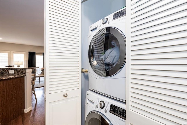 clothes washing area with dark hardwood / wood-style flooring and stacked washer and dryer