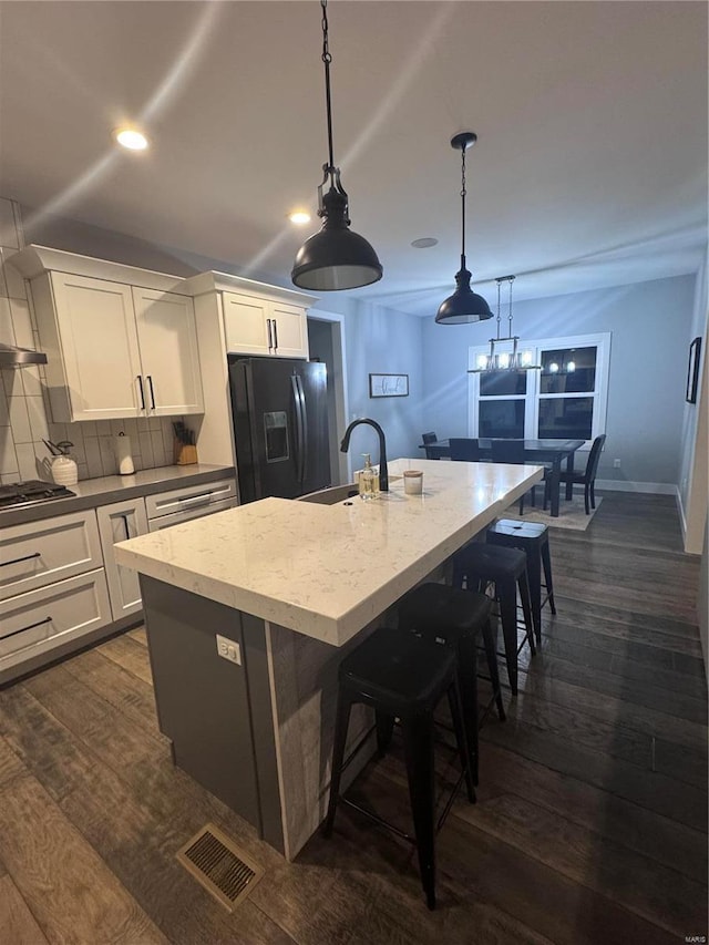 kitchen featuring sink, a kitchen island with sink, hanging light fixtures, white cabinets, and black refrigerator with ice dispenser