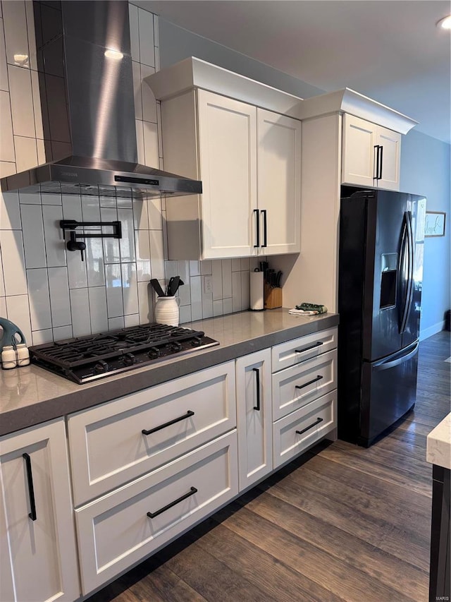 kitchen with white cabinets, decorative backsplash, black appliances, dark wood-type flooring, and wall chimney exhaust hood