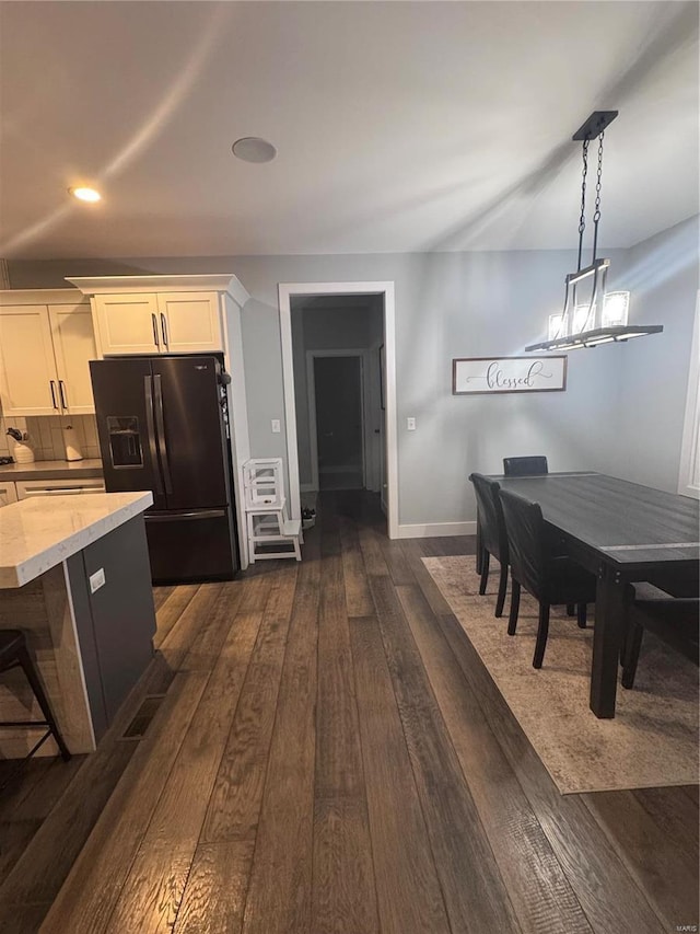 kitchen with dark hardwood / wood-style floors, white cabinetry, a kitchen breakfast bar, hanging light fixtures, and black fridge