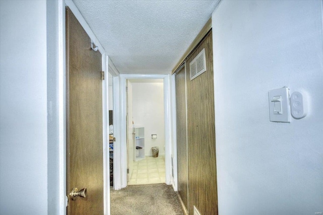 corridor with carpet floors, visible vents, and a textured ceiling