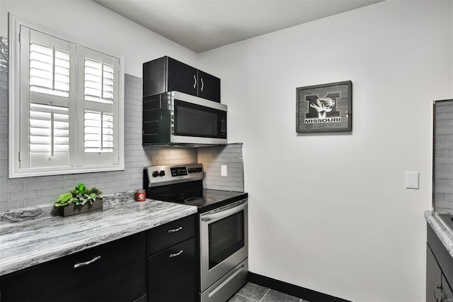 kitchen with tasteful backsplash, appliances with stainless steel finishes, dark tile patterned floors, and light stone counters