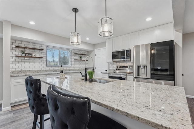 kitchen with appliances with stainless steel finishes, decorative light fixtures, white cabinetry, sink, and light stone counters