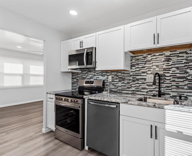 kitchen with sink, white cabinetry, light stone counters, tasteful backsplash, and stainless steel appliances