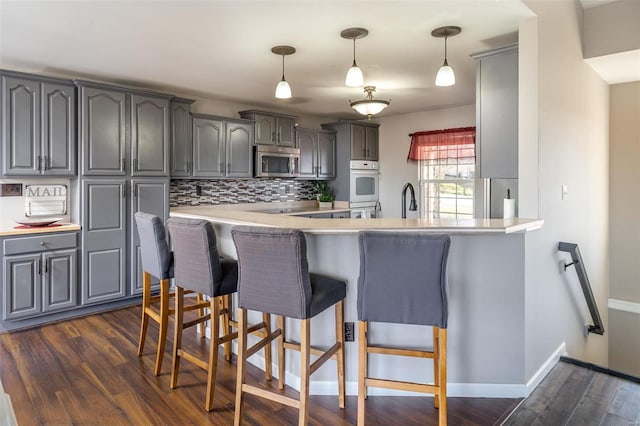 kitchen featuring gray cabinetry, backsplash, a kitchen breakfast bar, dark hardwood / wood-style floors, and kitchen peninsula