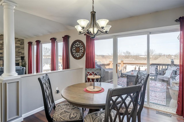 dining room with hardwood / wood-style flooring, a notable chandelier, vaulted ceiling, and ornate columns