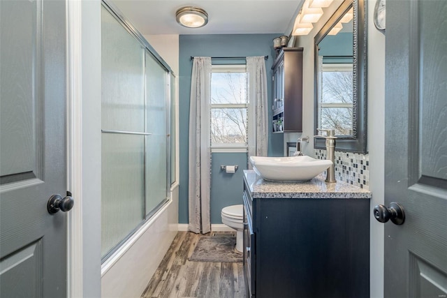 full bathroom featuring toilet, shower / bath combination with glass door, vanity, hardwood / wood-style flooring, and decorative backsplash