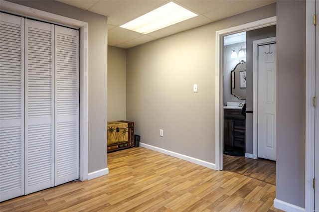 unfurnished bedroom featuring a paneled ceiling, ensuite bathroom, a closet, and light hardwood / wood-style flooring