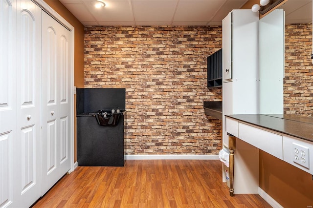 interior space featuring a paneled ceiling, light hardwood / wood-style floors, and brick wall