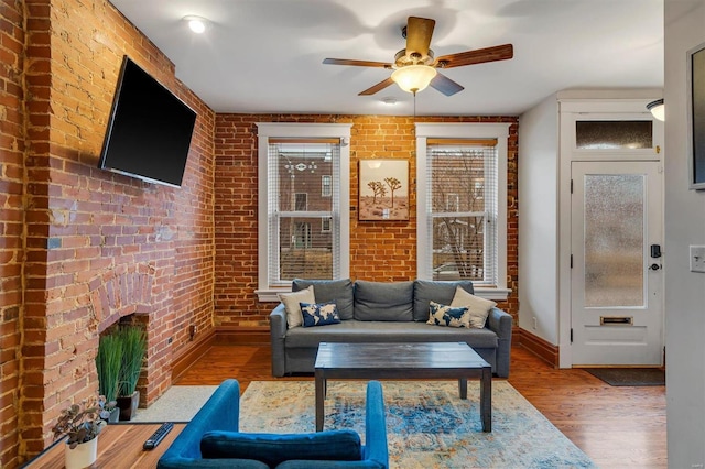 living room featuring a brick fireplace, hardwood / wood-style floors, ceiling fan, and brick wall