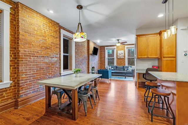 dining room with hardwood / wood-style floors, ceiling fan, and brick wall