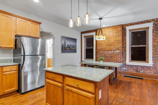 kitchen with hardwood / wood-style floors, decorative light fixtures, light stone countertops, and stainless steel refrigerator