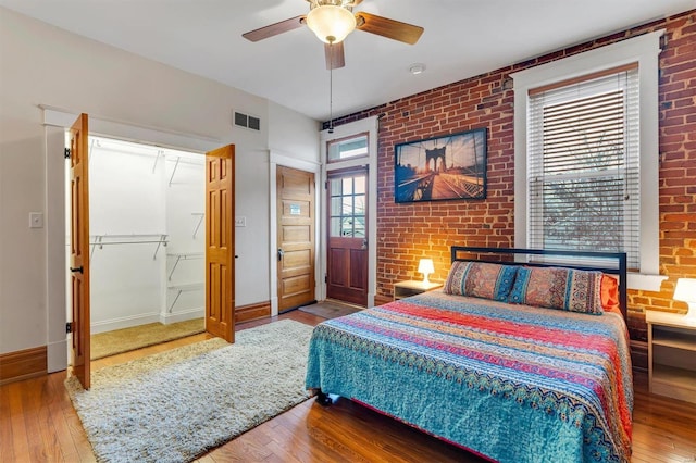 bedroom featuring hardwood / wood-style flooring, ceiling fan, and brick wall