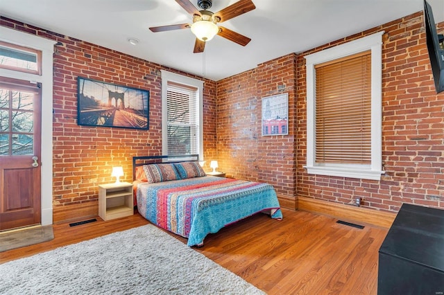 bedroom featuring hardwood / wood-style floors, ceiling fan, and brick wall