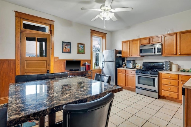 kitchen with a breakfast bar area, wood walls, light tile patterned floors, ceiling fan, and stainless steel appliances