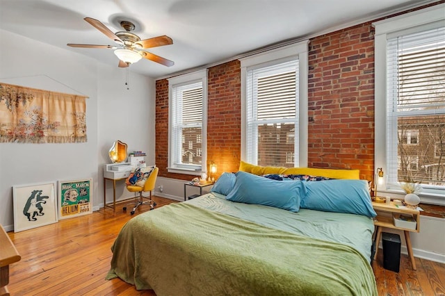 bedroom featuring ceiling fan, brick wall, hardwood / wood-style floors, and multiple windows