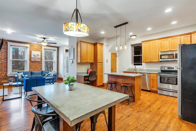 kitchen with a kitchen island, a breakfast bar, pendant lighting, stainless steel appliances, and light wood-type flooring